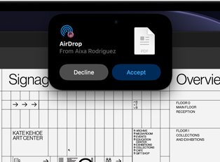 Egy kijelzőn a Dynamic Island AirDrop-kérést jelenít meg egy kis ablakban, a háttérben egy megnyitott Adobe Acrobat-fájllal.