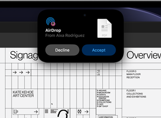 Egy kijelzőn a Dynamic Island AirDrop-kérést jelenít meg egy kis ablakban, a háttérben egy megnyitott Adobe Acrobat-fájllal.