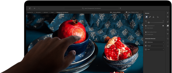 Csendéletfotó gránátalmákkal, kék kerámiaedényekkel és kék textíliákkal egy MacBook Pro PROLED XDR-kijelzőjén, egy kéz a kijelző felé nyúl, hogy megérintse a képet.