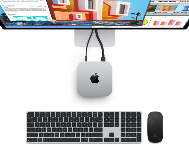 Ezüstszínű Mac mini felülnézetből, tetején az Apple logóval, monitorhoz csatlakoztatva, mellette vezeték nélküli Magic Keyboard és Magic Mouse.