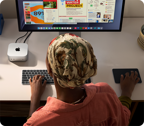 Íróasztalnál ülő ember egy Mac minin gépel, melyet Studio Displayjel, Magic Keyboarddal és Magic Trackpaddel használ, körülötte különféle tárgyak