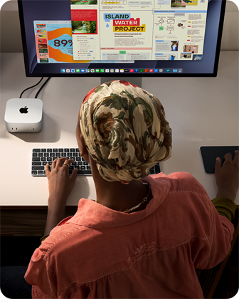 Íróasztalnál ülő ember egy Mac minin gépel, melyet Studio Displayjel, Magic Keyboarddal és Magic Trackpaddel használ, körülötte különféle tárgyak