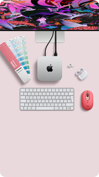 Mac mini felülnézetből, ezüstszínű alumíniumházzal, lekerekített sarkokkal, középen fényes fekete Apple-logóval, kábellel csatlakoztatva, a képen felül egy Studio Display egy része, kinyitott fedelű AirPods 4, Pantone-színminták, számbillentyűzetes billentyűzet és egér