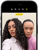 Fekete iPhone 18 Pro elölnézetből, a kijelzőn két modell pózol a kamerának, bemutatva a Center Stage előlapi kamerát