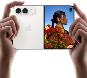 Vízszintes tájolású iPhone csillagfehér színben, két kézben tartva, kinyitva, a bal oldali panelen a 48 MP Dual Fusion hátlapi kamerák, a jobb oldali panelen egy külső kijelzőn fotózkodó ember, aki felvételkészítés közben láthatja a saját arcát a Duo Preview funkcióval.