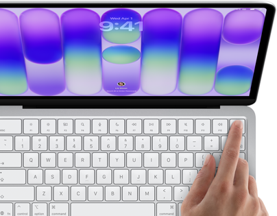 MacBook Neo ezüstszínben, a kijelzőn a bejelentkezési képernyő, egy ember ujja a billentyűzet jobb felső sarkában található Touch ID érzékelőn