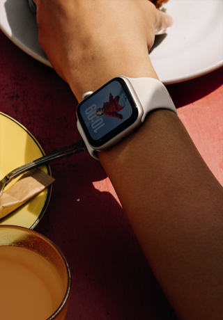 Egy ember a tányérján lévő reggeliért nyúl, Apple Watch SE 3-at visel a csukóján csillagfény alumíniumtokkal, mindig bekapcsolt kijelzővel, a számlapján egy portréval, csillagfény sportszíjjal