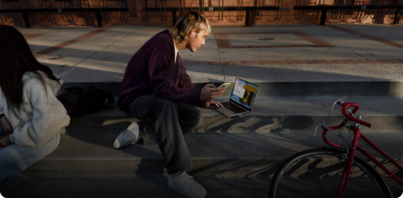 Egy lépcsőn ülő személy a szabadban egyszerre használ egy MacBookot akkumulátorról és egy iPhone-t